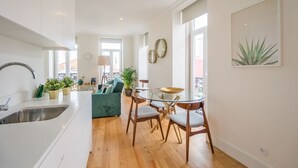 A modern kitchen with a sink, dining area with chairs, and a glass table. There is a sofa and a plant in the living area.