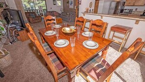 A dining area with a wooden table set for six, surrounded by plaid-patterned chairs.