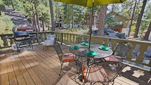 A wooden deck with a round table and chairs, a grill, and a yellow umbrella.