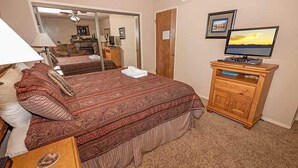 A bedroom with a large bed, a wooden dresser, a television, and a mirror.