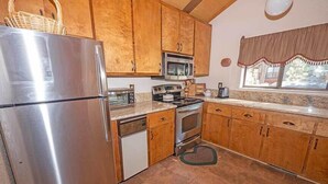 A kitchen with wooden cabinets, a stainless steel refrigerator, a microwave, an oven, and a sink.