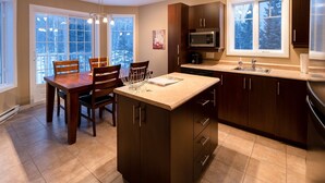 Une cuisine moderne avec des meubles de couleur bois foncé, un réfrigérateur en acier inoxydable, un four à micro-ondes et une grande fenêtre offrant une vue sur l’extérieur.