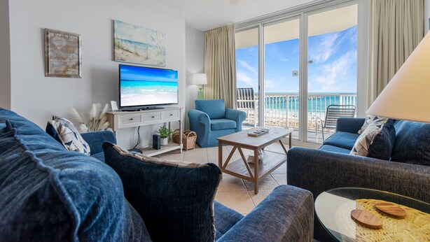 Un salón amplio con un televisor grande, asientos cómodos, una mesa de centro y un balcón con vista a la playa.