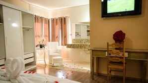 Une chambre d’hôtel avec un lit, une chaise, un bureau, une télévision et une salle de bain visible à travers une porte ouverte.