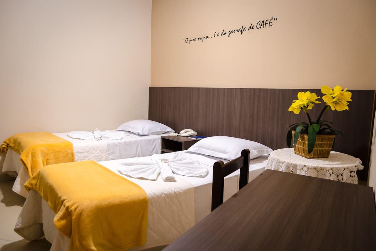 Une chambre d’hôtel avec deux lits, une petite table, un vase avec des fleurs et une citation affichée sur le mur.