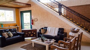Un salon chaleureux avec deux canapés en cuir noir, une table basse en bois et un escalier doté d’une rampe en métal.
