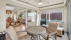 A spacious living area with a round table, comfortable seating, a ceiling fan, and large windows offering a view of the outdoors. - Lake View Villa with a 1 Car Garage, 2 Bedrooms in Lakeside of Naples, Fl (Naples)