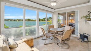 A sunlit room with a view of a lake, a ceiling fan, and a dining area with chairs and a table. - Lake View Villa with a 1 Car Garage, 2 Bedrooms in Lakeside of Naples, Fl (Naples)