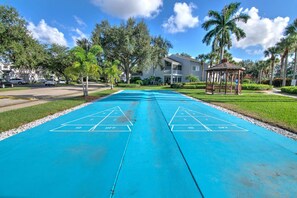 A blue shuffleboard court with a gazebo and palm trees in the background. - Lake View Villa with a 1 Car Garage, 2 Bedrooms in Lakeside of Naples, Fl (Naples)