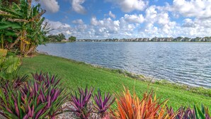 A lakeside view with a grassy area and colorful plants in the foreground. - Lake View Villa with a 1 Car Garage, 2 Bedrooms in Lakeside of Naples, Fl (Naples)