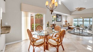 A spacious living area with a glass dining table surrounded by wicker chairs, a modern chandelier, and a ceiling fan. - Lake View Villa with a 1 Car Garage, 2 Bedrooms in Lakeside of Naples, Fl (Naples)