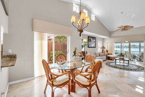 A spacious living area with a glass dining table surrounded by wicker chairs, a modern chandelier, and a ceiling fan. - Lake View Villa with a 1 Car Garage, 2 Bedrooms in Lakeside of Naples, Fl (Naples)