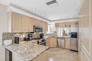 A modern kitchen with granite countertops, stainless steel appliances, and light wood cabinetry.