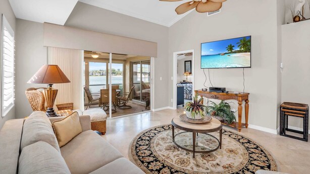 A spacious living room with a large ceiling fan, a flat-screen TV, and a view of the outdoors through a sliding glass door. - Lake View Villa with a 1 Car Garage, 2 Bedrooms in Lakeside of Naples, Fl (Naples)