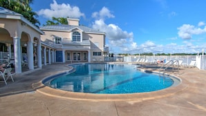 A large swimming pool with a curved edge, surrounded by lounge chairs and a covered patio area. - Lake View Villa with a 1 Car Garage, 2 Bedrooms in Lakeside of Naples, Fl (Naples)