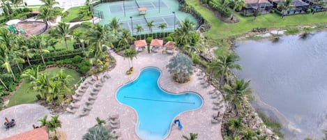 A residential area with a swimming pool surrounded by lounge chairs and palm trees.