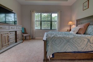 A bedroom with a bed, a dresser, a window with curtains, and a lamp.