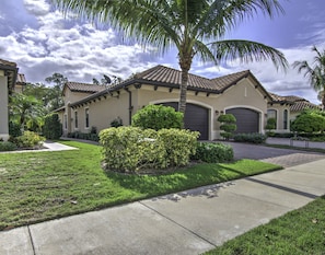 A residential house with a well-maintained lawn, palm trees, and a driveway leading to a garage.