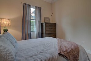 Un dormitorio con cama, cómoda, lámpara y ventana con cortinas.
