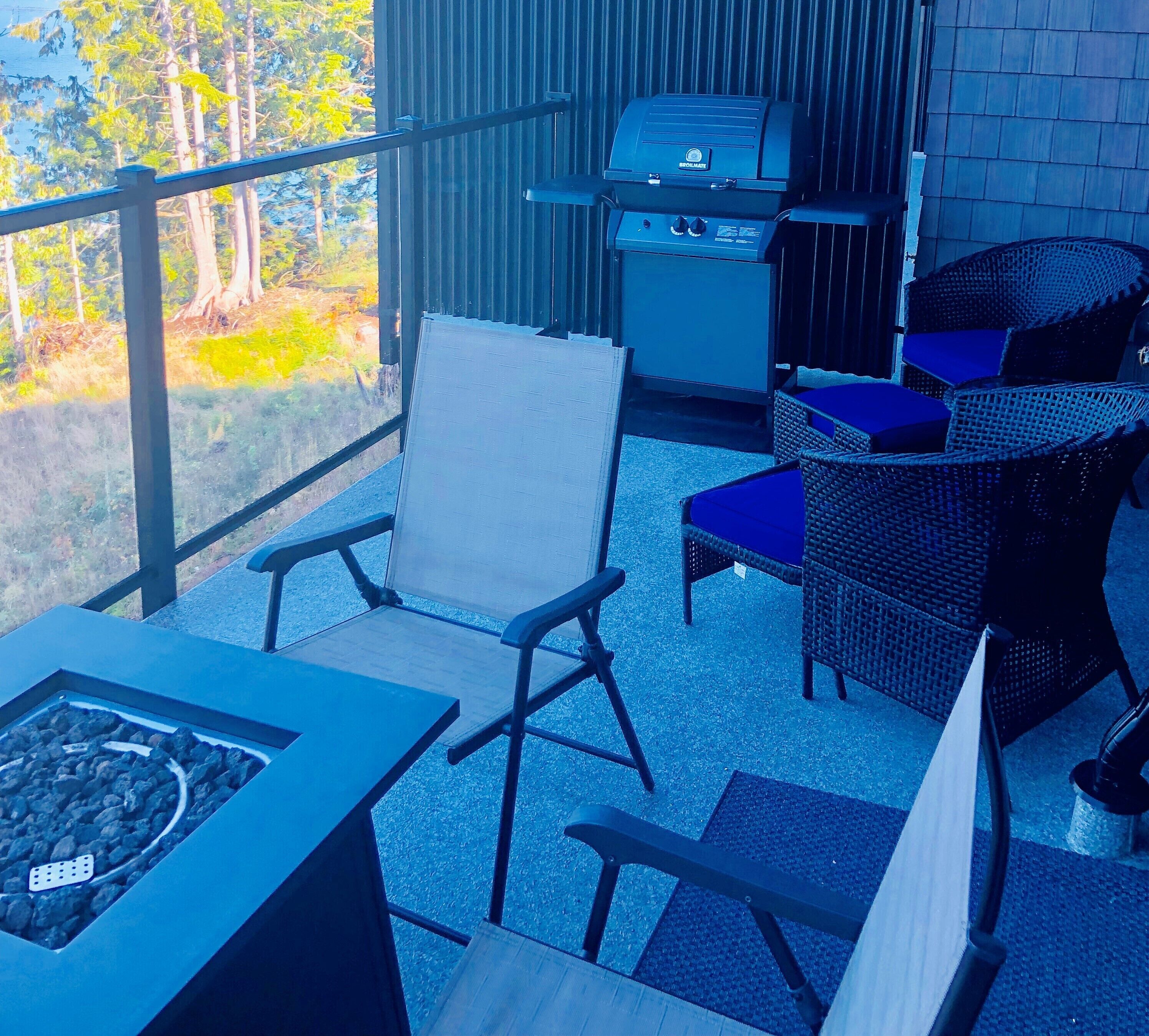 Een balkon met een barbecue, rieten stoelen en een tafel met een vuurplaats.