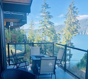 En balkon med et bord og stole med udsigt over en sø og skov.