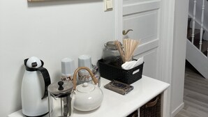 A kitchen counter with a coffee maker, teapot, and jars. A framed coffee advertisement hangs on the wall.