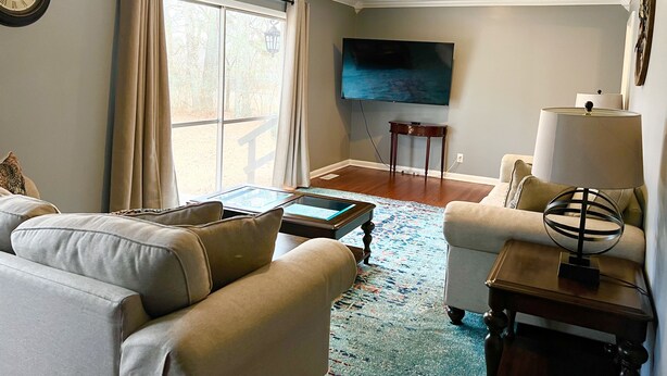 A living room with a sofa, armchair, coffee table, and a TV mounted on the wall.