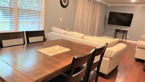 A dining area with a wooden table and chairs, a sofa, and a television on the wall.