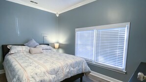 A bedroom with a bed, a ceiling fan, a window with blinds, and a nightstand.