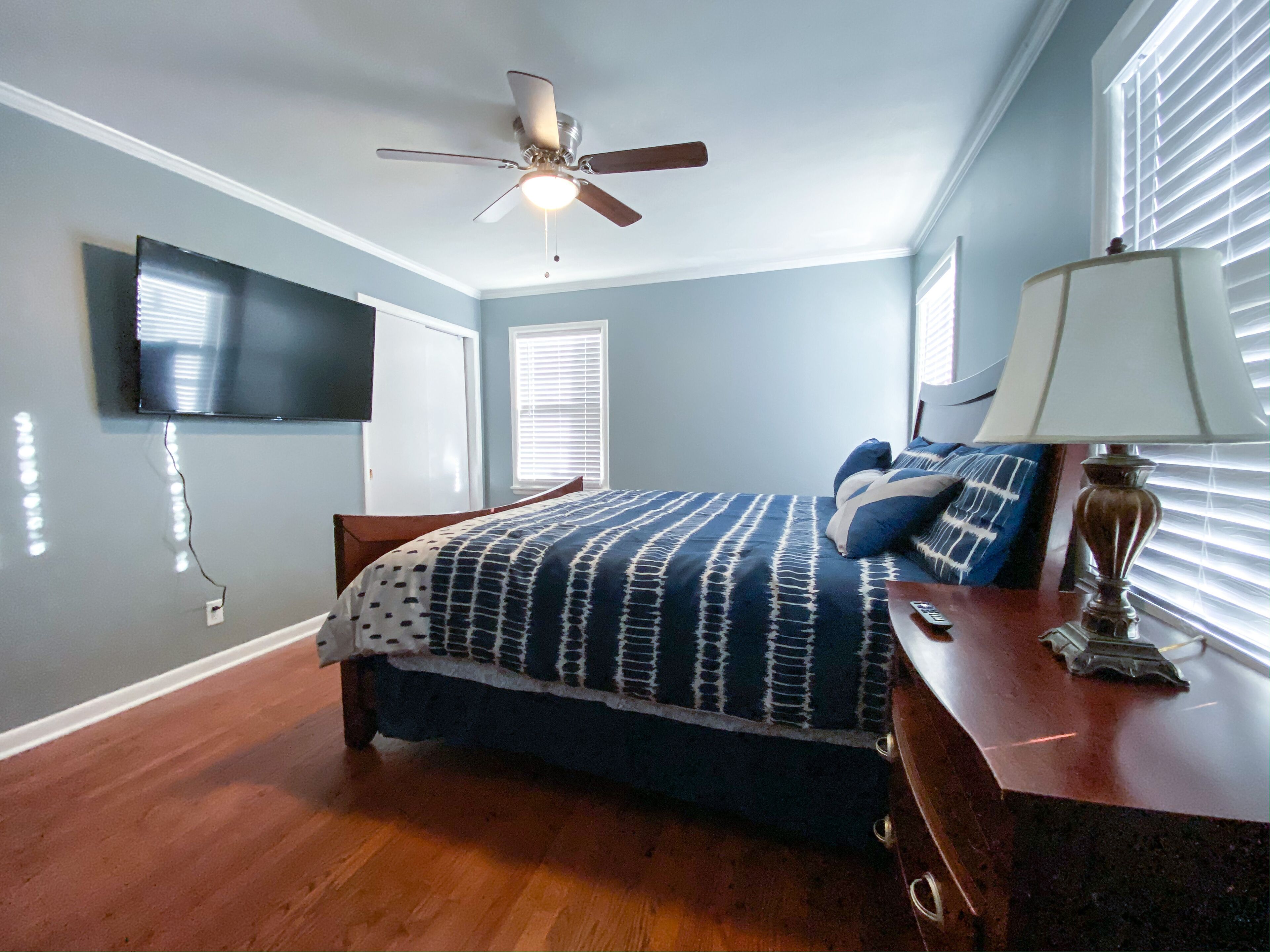 A bedroom with a bed, a ceiling fan, a TV mounted on the wall, and a window with blinds.