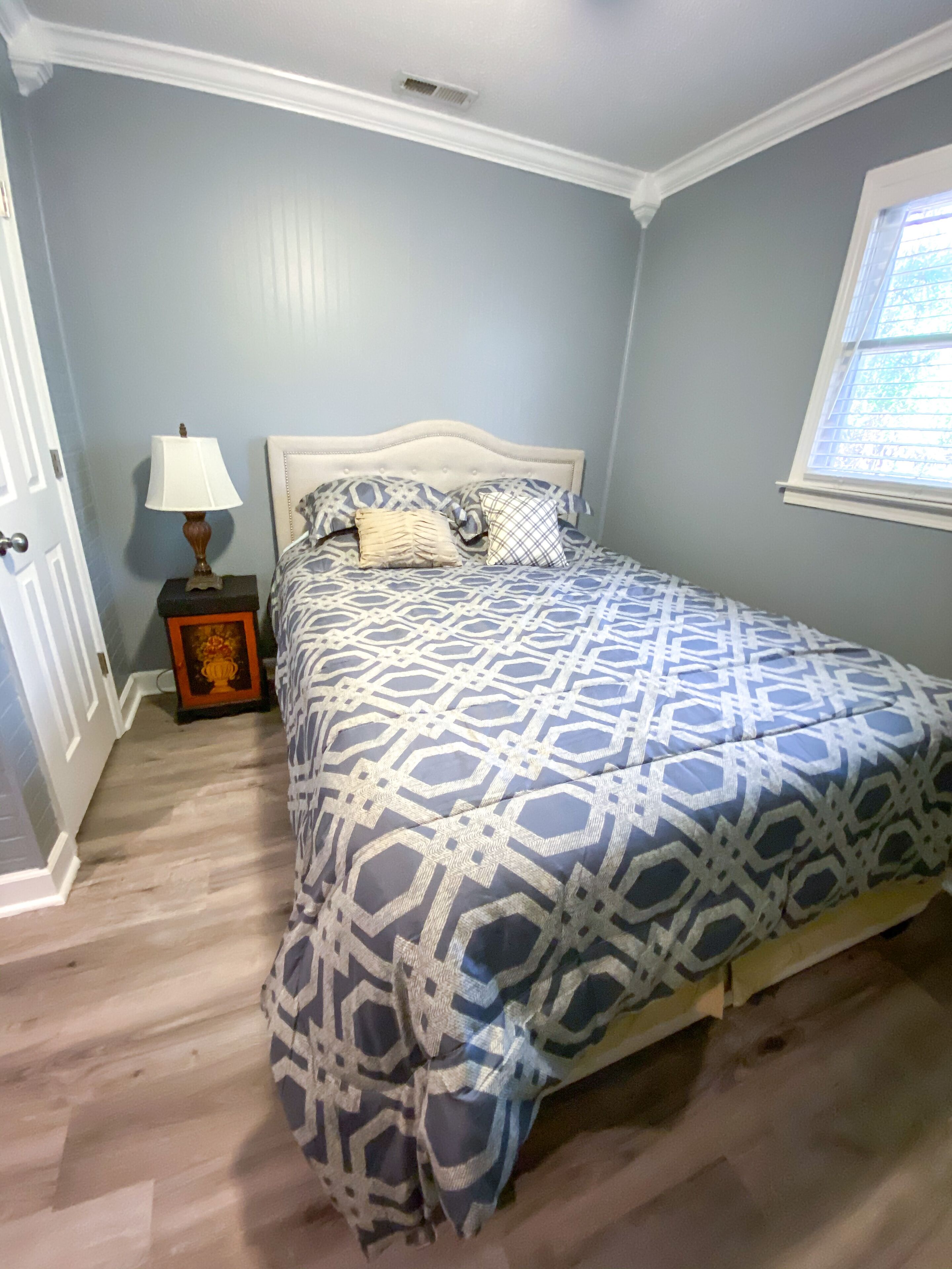 A bedroom with a bed, a nightstand, a lamp, and a window.