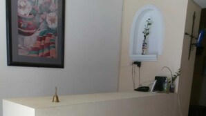 A reception desk with a framed picture above it, a small window with a plant, and a bell on the desk. - Mayan Hotel Boutique (Mérida)