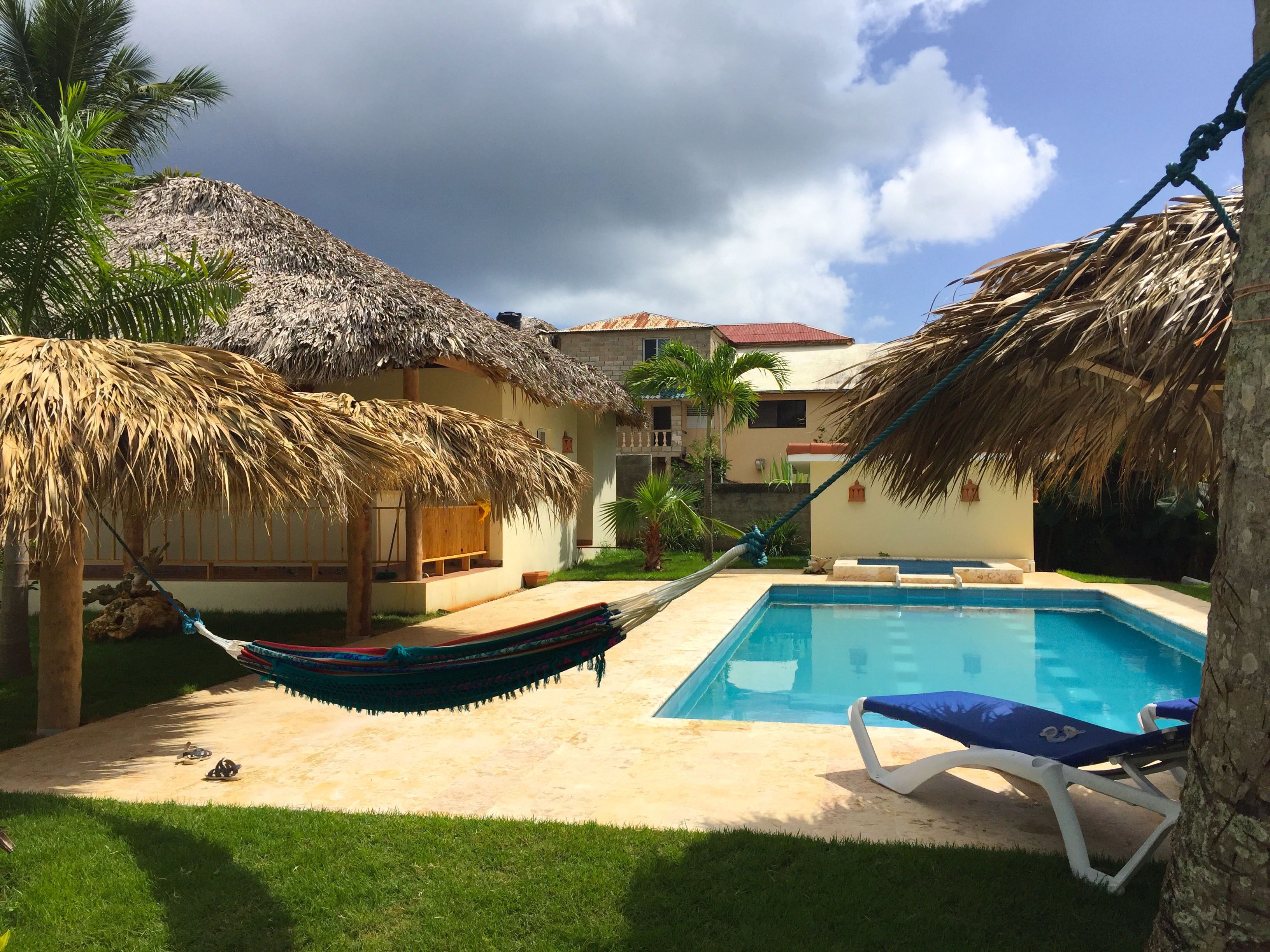 A pool area with a hammock, lounge chairs, and thatched-roof structures.