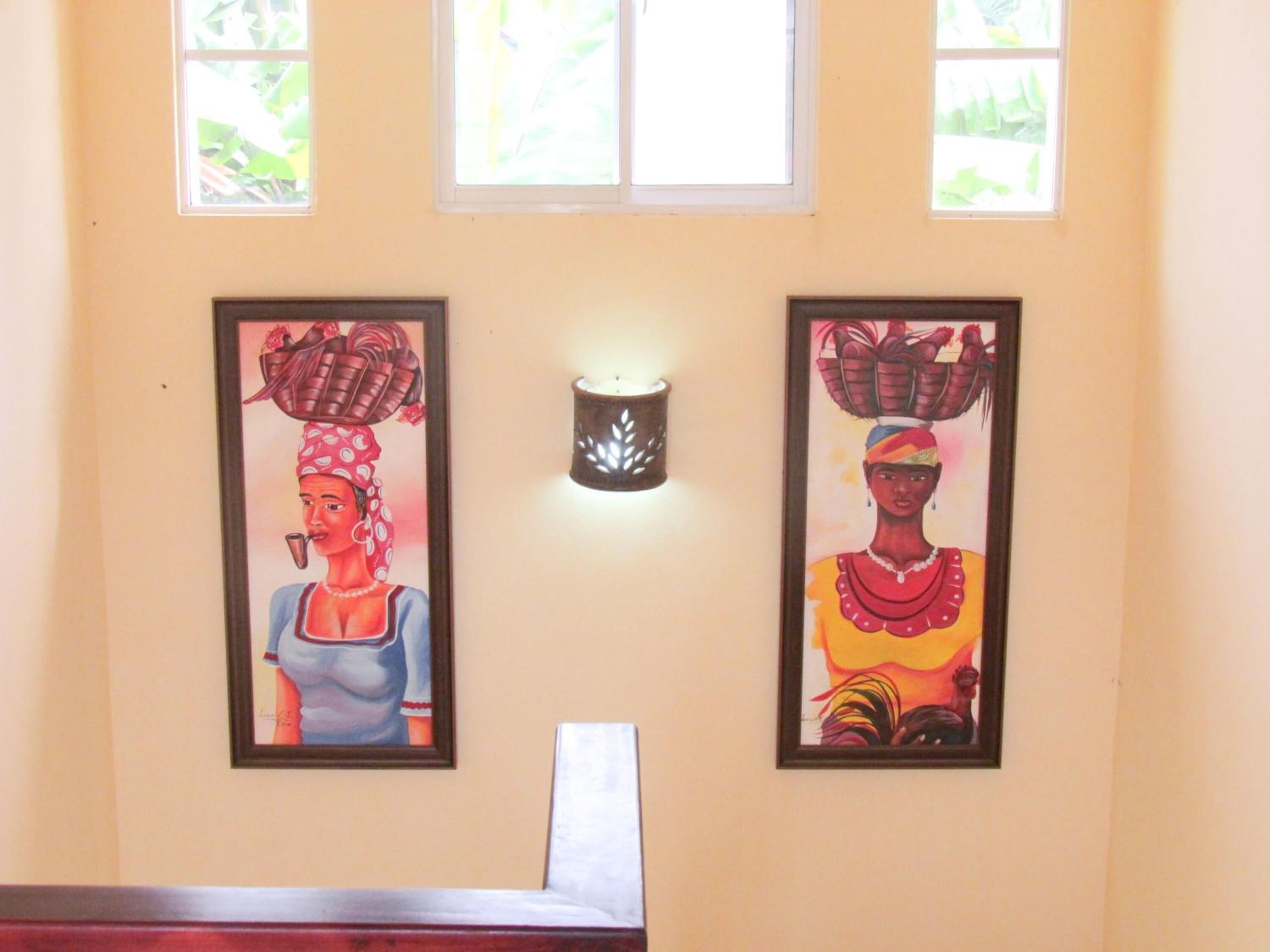 Two framed paintings on a wall, a wall-mounted light fixture, and a window with a view of greenery.