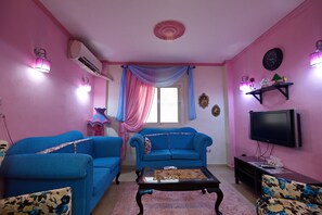 A living room with two blue sofas, a coffee table, a TV, and pink walls.