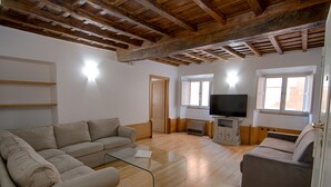 Ein Wohnzimmer mit Holzboden, einem beigefarbenen Sofa, einem Glastisch und einem Fernseher auf einer Holzkommode.