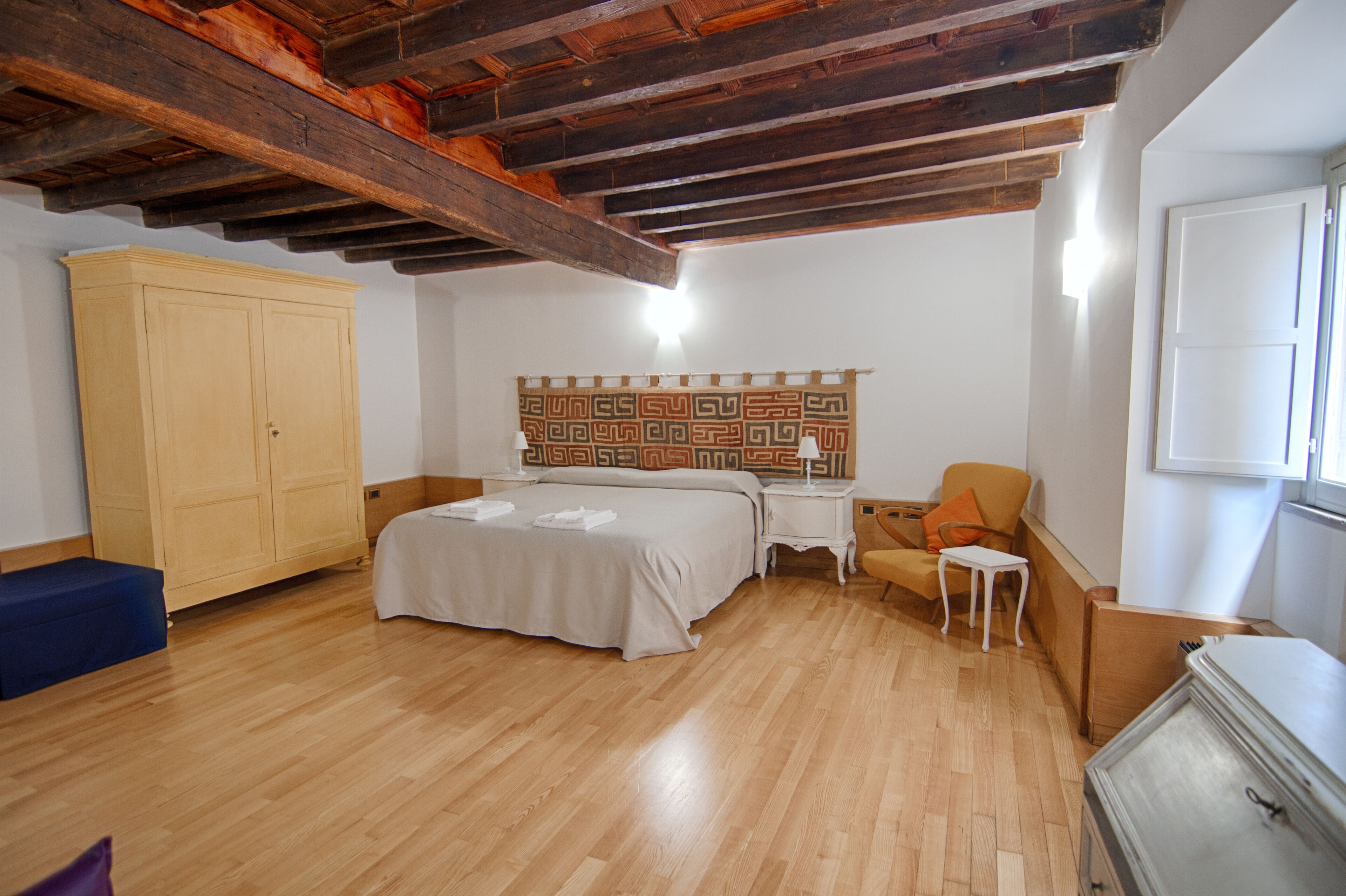 A bedroom with a wooden ceiling, a bed, a wardrobe, a chair, and a small table.