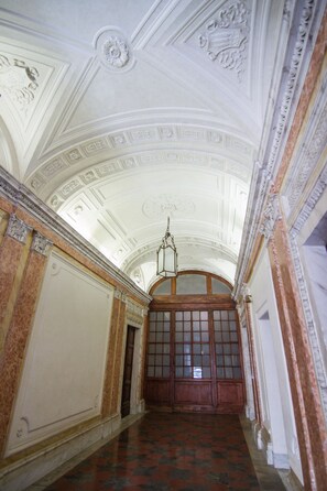 A grand hallway with ornate ceiling details, a large wooden door, and patterned flooring. - Rinidia Roma Centro (Rome)