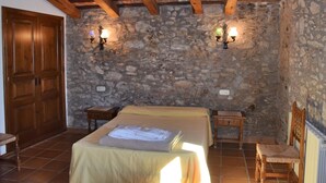 Una camera da letto con parete in pietra, travi in legno, un letto, una sedia e due lampade a parete.