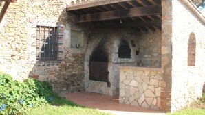 Un edificio in pietra con una zona cucina esterna rustica, comprensiva di un forno in pietra e un pergolato in legno.