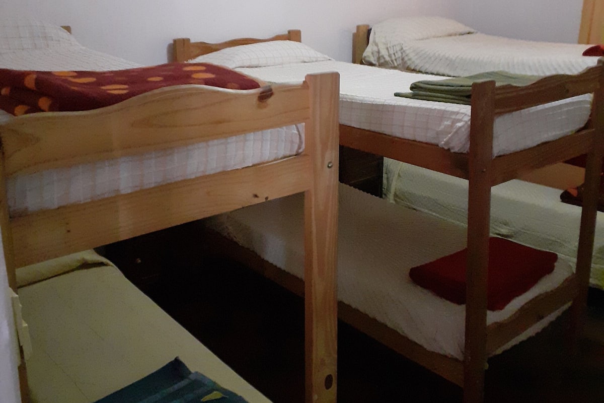 Una habitación con dos literas, un cabecero de madera, una pared blanca y dos cuadros abstractos.