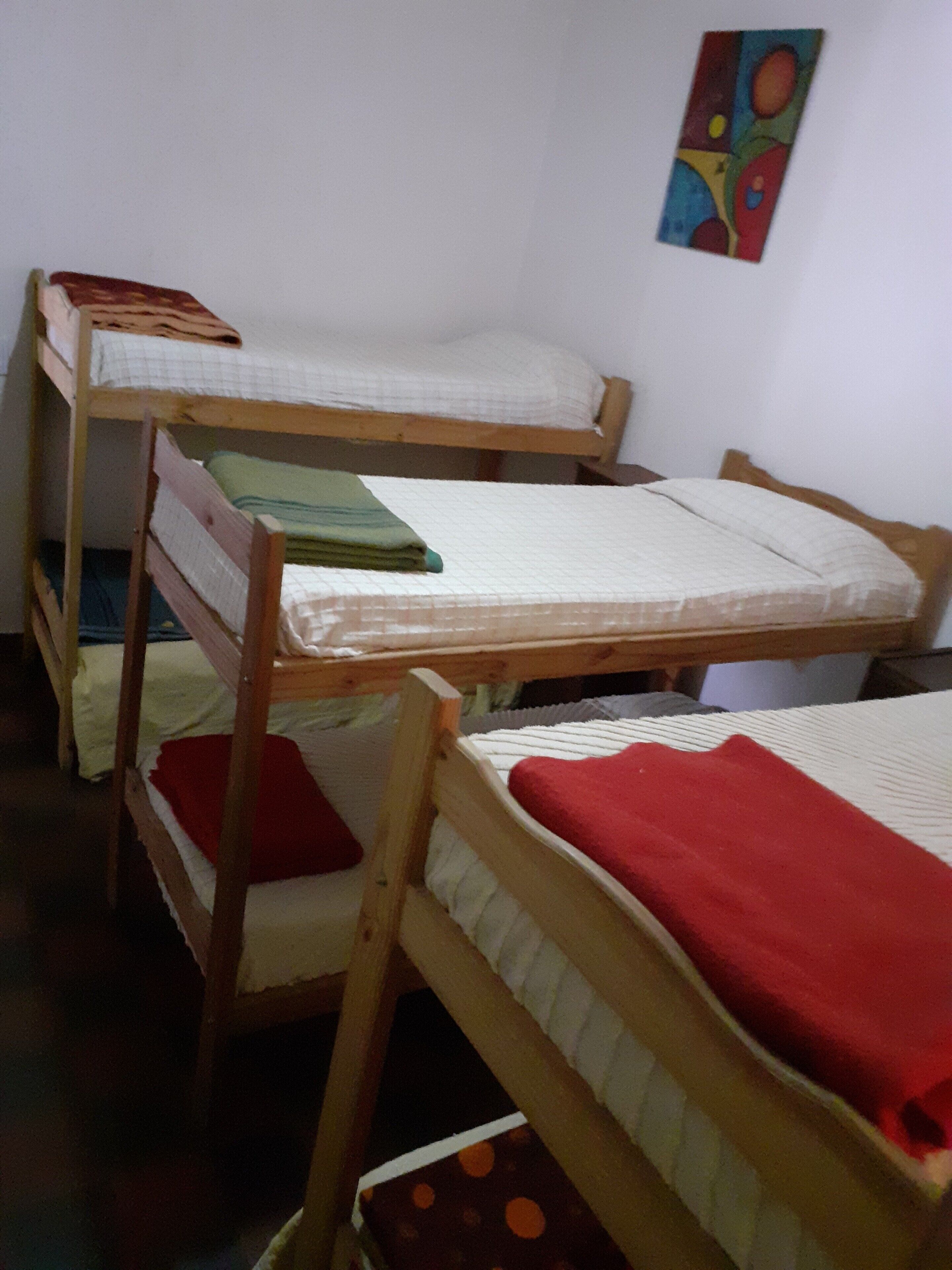 A dormitory room with bunk beds, a small table, and a colorful painting on the wall.