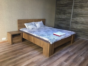 A wooden bed with a patterned bedspread, a nightstand, and a wooden wall.