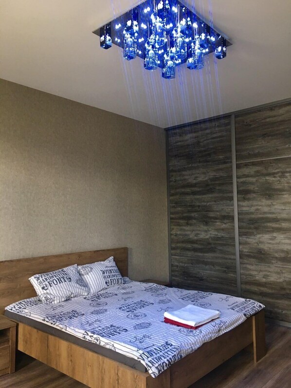 A modern bedroom with a wooden bed, a patterned bedspread, and a unique blue chandelier.