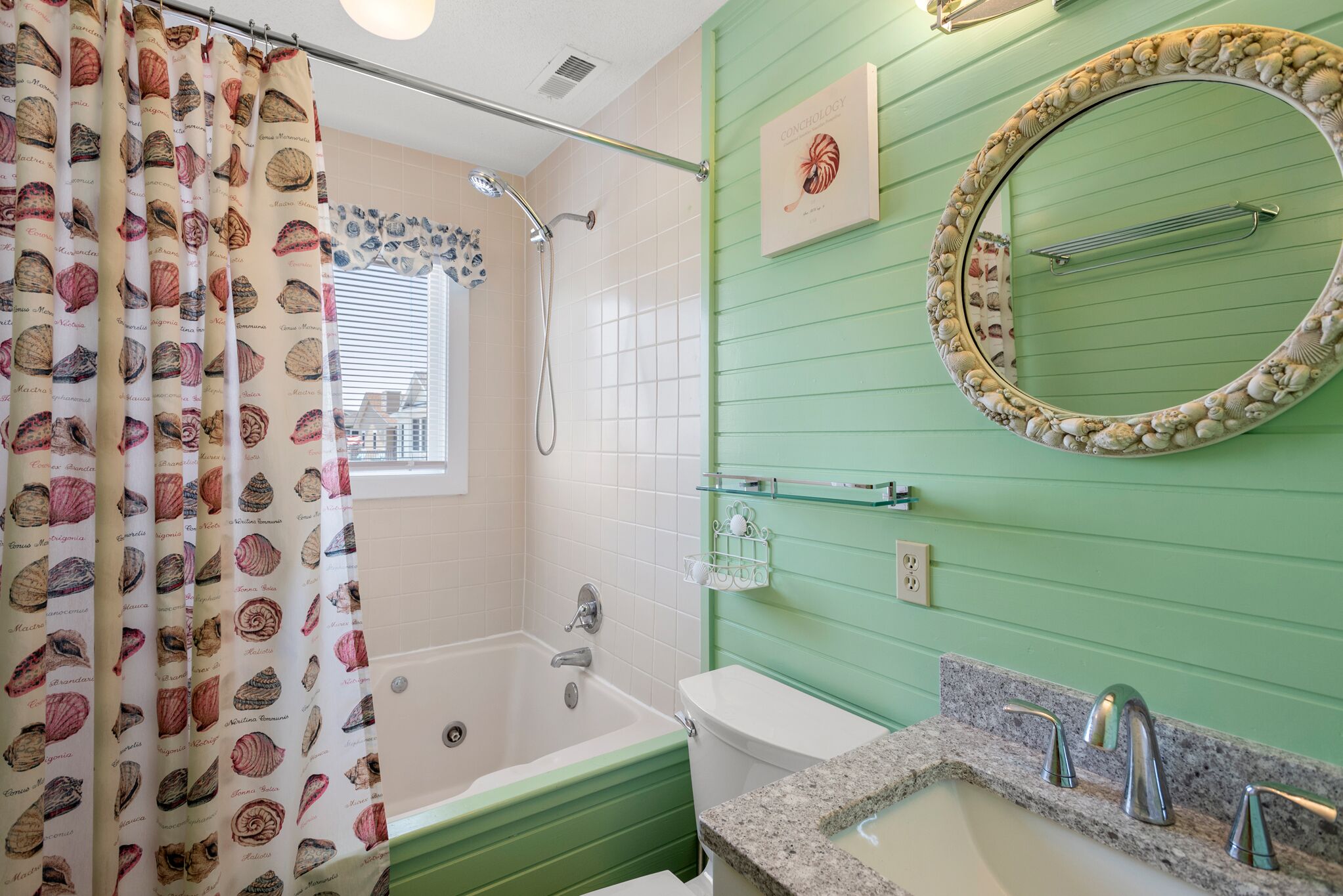Een badkamer met een groene wand, een ronde spiegel met schelpenlijst, een badkuip en een douche.
