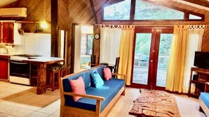 Una cabaña acogedora con interior de madera, un sofá, una mesa de comedor y una zona de cocina.
