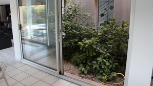 Un intérieur moderne avec une porte-fenêtre coulissante donnant sur un balcon agrémenté d’un petit jardin et d’un tuyau d’arrosage jaune.