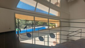 Une pièce dotée d’une grande verrière, offrant une vue sur une piscine et donnant sur un balcon avec une balustrade.