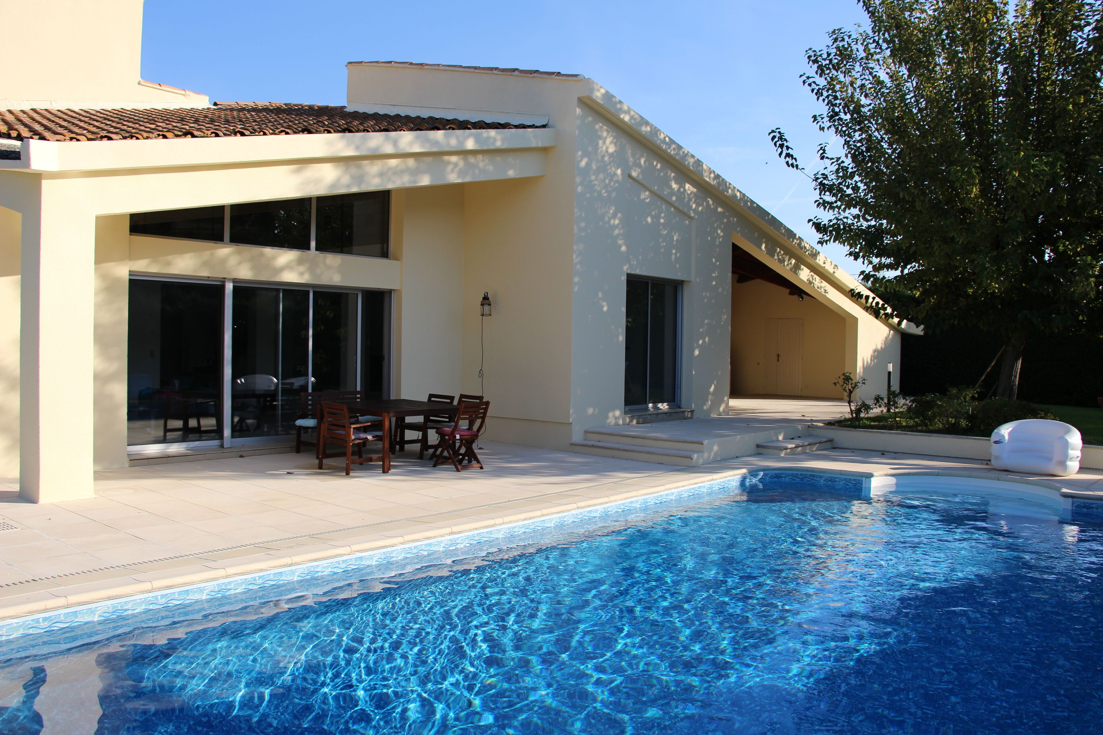 Una casa moderna con piscina, un patio con mobiliario exterior y un amplio ventanal con vistas a la piscina.