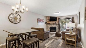 A modern living room with a stone fireplace, a dining area with a wooden table and bar stools, and a comfortable seating area with a sofa and armchairs.
